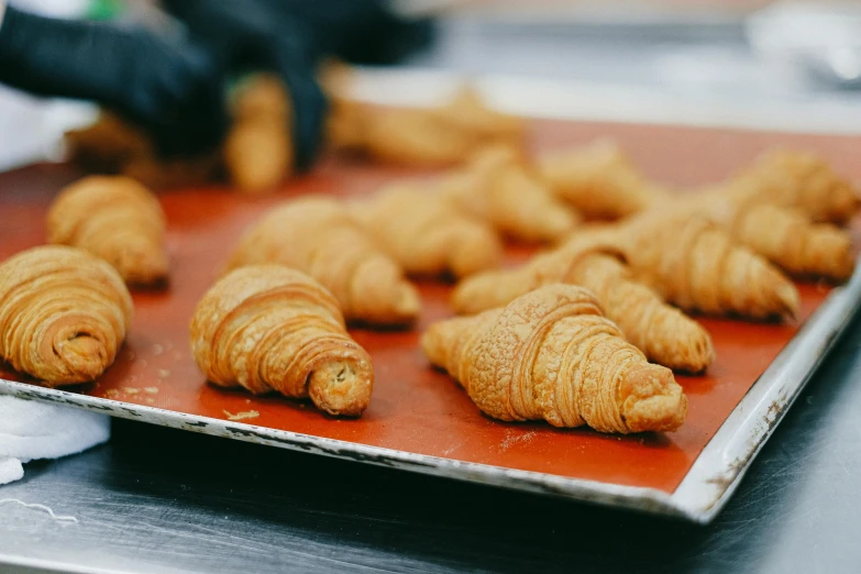 a tray that has some croissants on it, pexels contest winner, cone shaped, larvae, hands on counter, finely textured