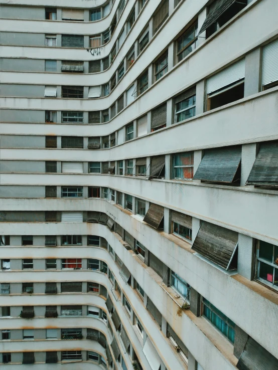 a very tall building with lots of windows, inspired by Ned M. Seidler, unsplash contest winner, brutalism, crenellated balconies, photo of poor condition, shutters, curvilinear perspective