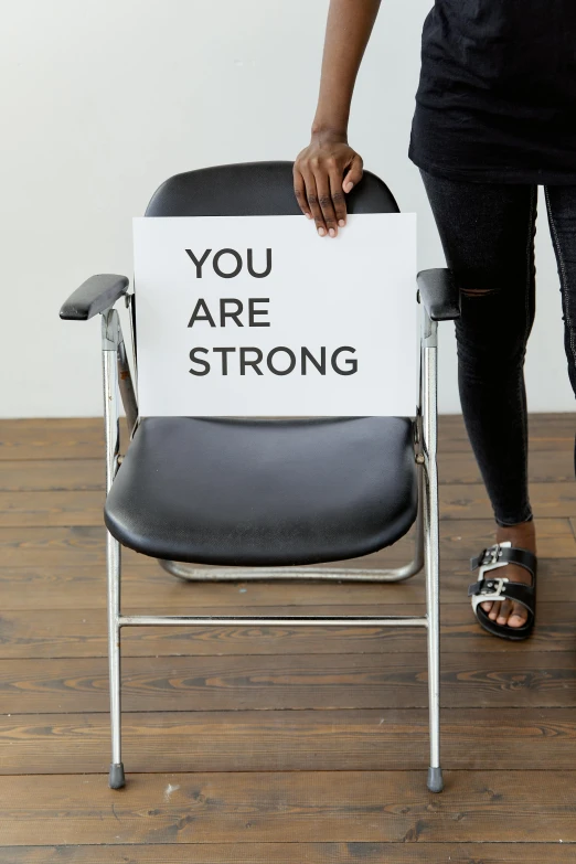 a woman holding a sign that says you are strong, chair, profile image, full frame image, large)}]