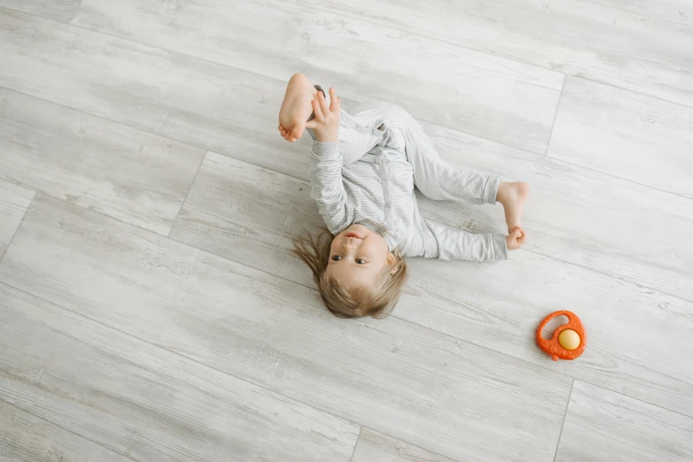 a little girl laying on the floor playing with a toy, pexels contest winner, arabesque, white wood, background image, grey, perfectly tileable