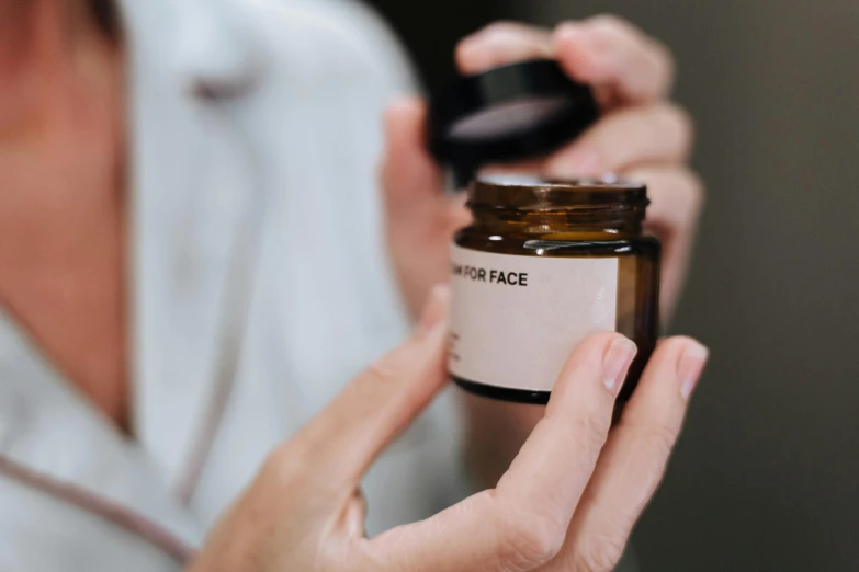 a close up of a person holding a jar of cream, by Julia Pishtar, pexels contest winner, bauhaus, perfect face template, apothecary, label, small in size