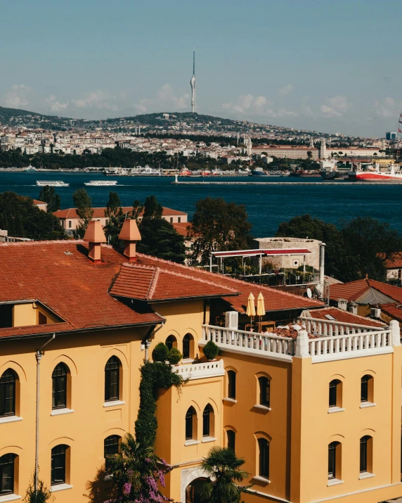 a large yellow building sitting next to a body of water, a colorized photo, pexels contest winner, turkish and russian, city in the distance, background image, cornucopia