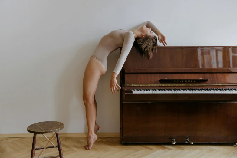 a woman standing next to a piano in a room, pexels contest winner, arabesque, wearing leotard, bending over, amazingly composed image, ad image