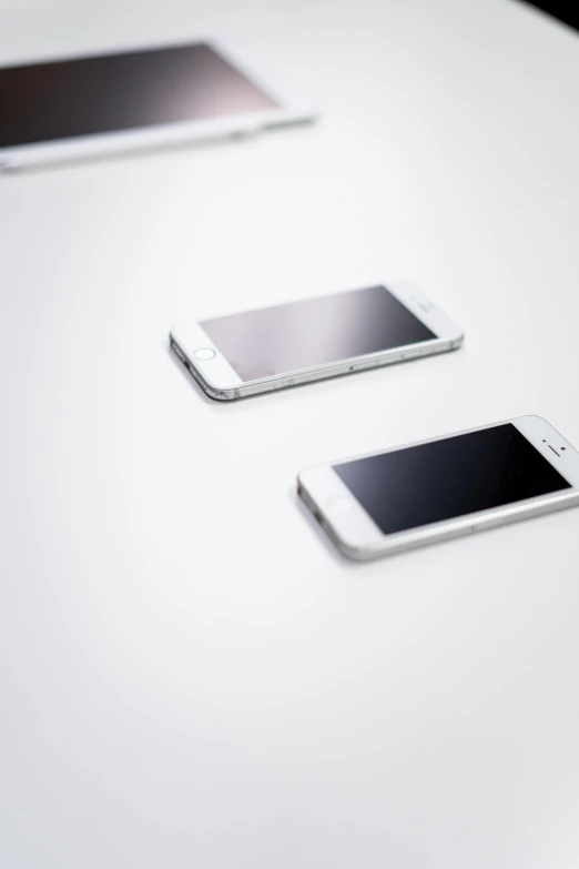 three cell phones sitting on top of a white table, by Simon Gaon, gradient white to silver, ap news photo, two, vine