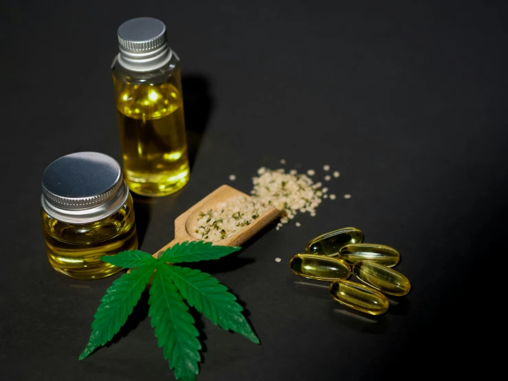 a close up of a bottle of oil with a marijuana leaf next to it, by Julia Pishtar, pexels, alien capsules, with a black background, 3 heads, a wooden