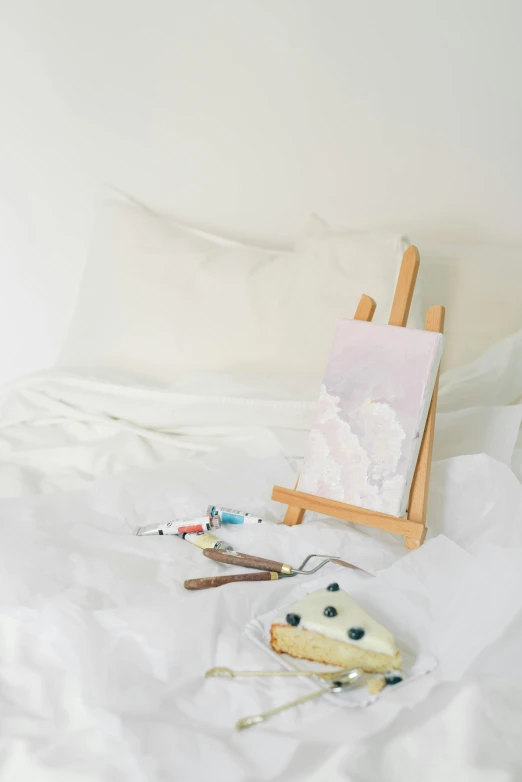 an easel sitting on top of a bed next to a painting, inspired by Emil Carlsen, trending on unsplash, cake art, white, miniature product photo, small