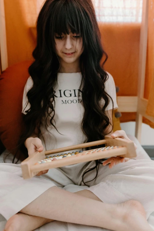 a woman sitting on a bed reading a book, an album cover, by Sengai, trending on pexels, long weaving brown hair, wooden art toys, black haired girl wearing hoodie, loom