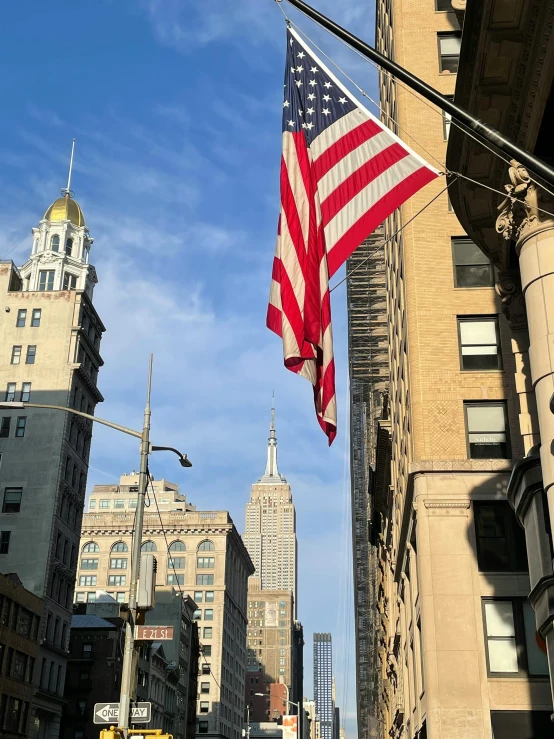 a large american flag hanging from the side of a tall building, buildings in the distance, photo on iphone, 🚿🗝📝, 8 k image