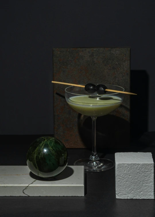 a martini sitting on top of a table next to a watermelon, a still life, inspired by Carlo Martini, unsplash, suprematism, hans bellmer and nadav kander, detailed product image, obsidian globe, hiroshi sugimoto