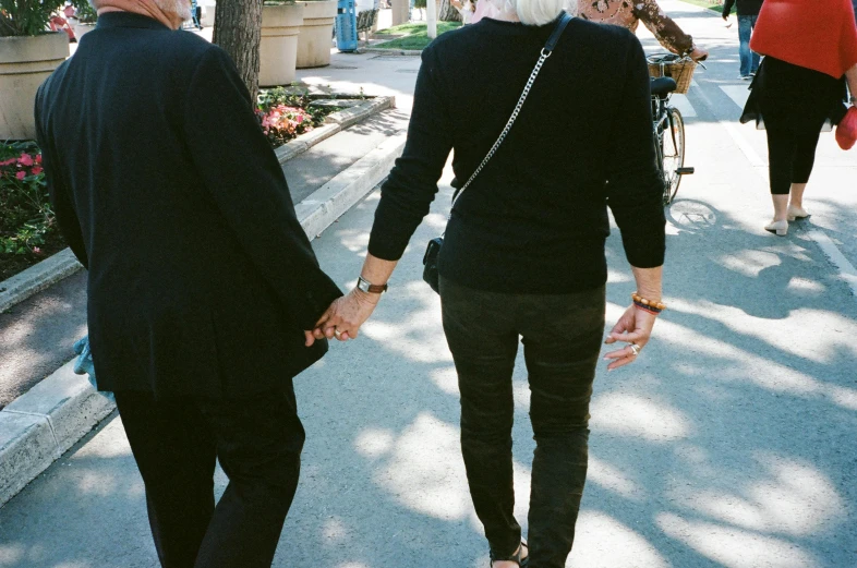 a man and woman walking down a sidewalk holding hands, unsplash, antipodeans, older woman, leather cuffs around wrists, lgbt, eva elfie