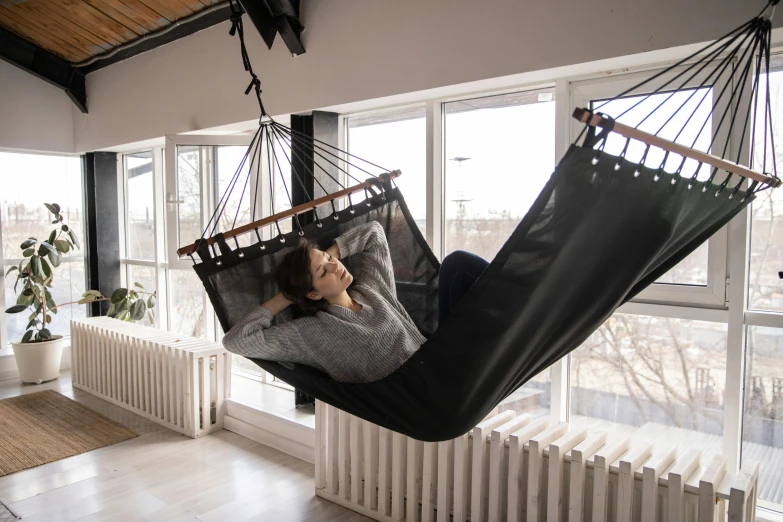 a woman laying in a hammock in a room, inspired by Bela Čikoš Sesija, unsplash, arabesque, black armchair, with screens and silks, balcony, anthracite