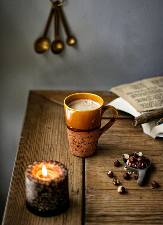 a cup of coffee sitting on top of a wooden table, a still life, by David Garner, hurufiyya, candles, thumbnail, warm cosy colors, product display photograph