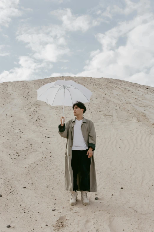 a woman standing in the sand holding an umbrella, inspired by Russell Dongjun Lu, unsplash, conceptual art, handsome man, jungkook, asian male, wearing off - white style