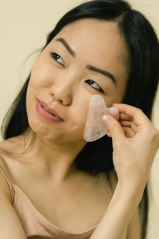 a woman putting a face mask on her face, an album cover, trending on pexels, mingei, rose quartz, asian face, tear drop, translucent