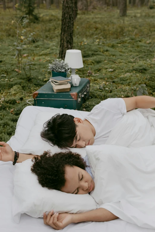 a couple of people laying on top of a bed, in the grass, sleeping, with a twin, cozy setting