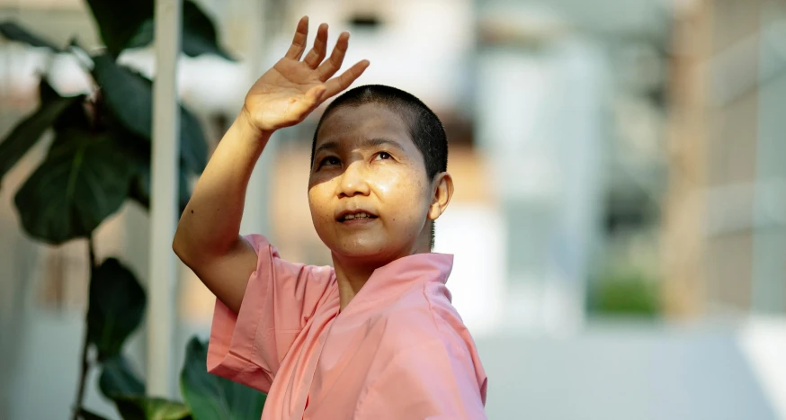 a young boy in a pink shirt holding his hand up, inspired by Ma Quan, pexels contest winner, happening, buddhist monk, avatar image, asian woman, close - up photo