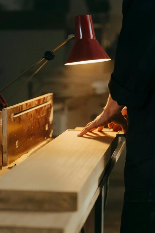 a person cutting a piece of wood on a table, by Haukur Halldórsson, accent lighting, uplit, gilding, unbeatable quality