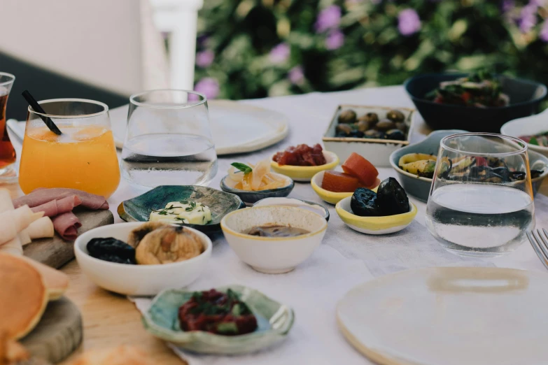 a table topped with plates of food and drinks, unsplash, hurufiyya, olive trees, grey, background image, middle eastern skin