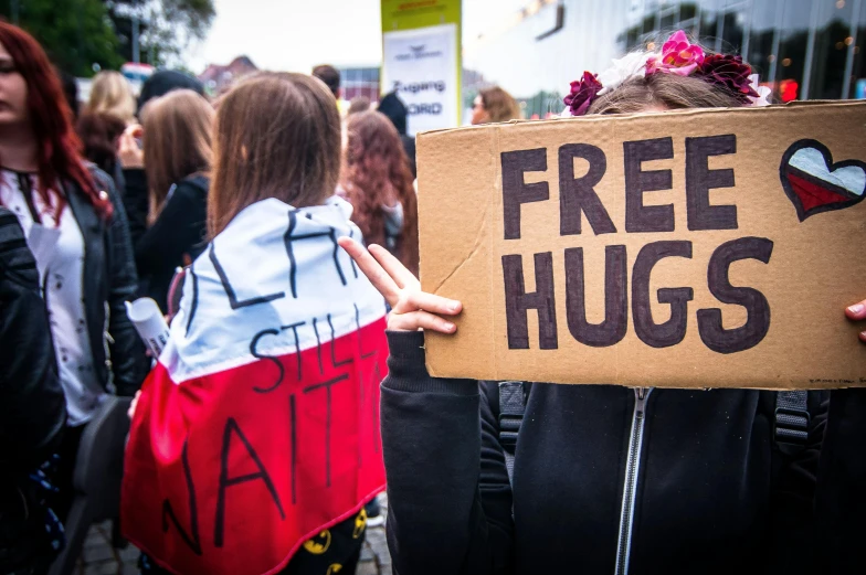 a person holding a sign that says free hugs, by Julia Pishtar, girls, ewa juszkiewicz, thumbnail, high quality image