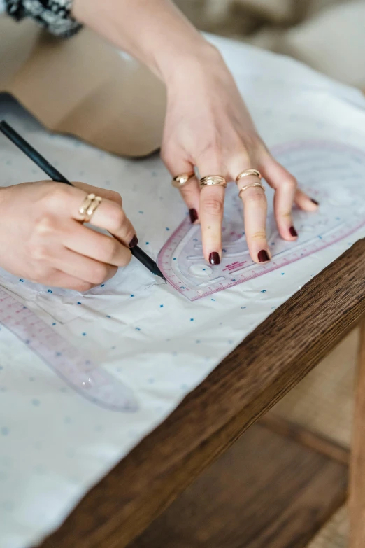 a woman is drawing on a piece of paper, a cross stitch, by Julia Pishtar, trending on pexels, intricate silk clothing, measurements, multi-part, gold detailed line work