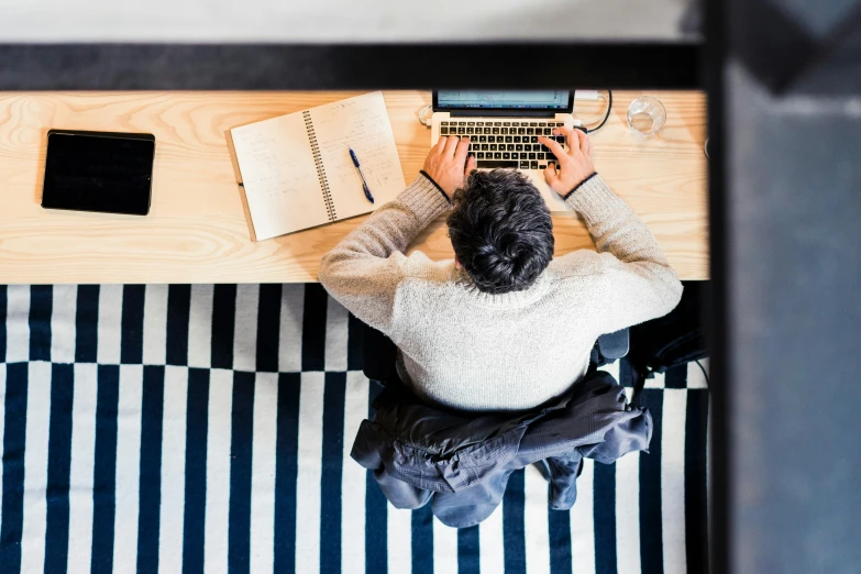 a man sitting at a table working on a laptop, by Julia Pishtar, pexels, arbeitsrat für kunst, wide high angle view, 9 9 designs, backfacing, 1 2 9 7