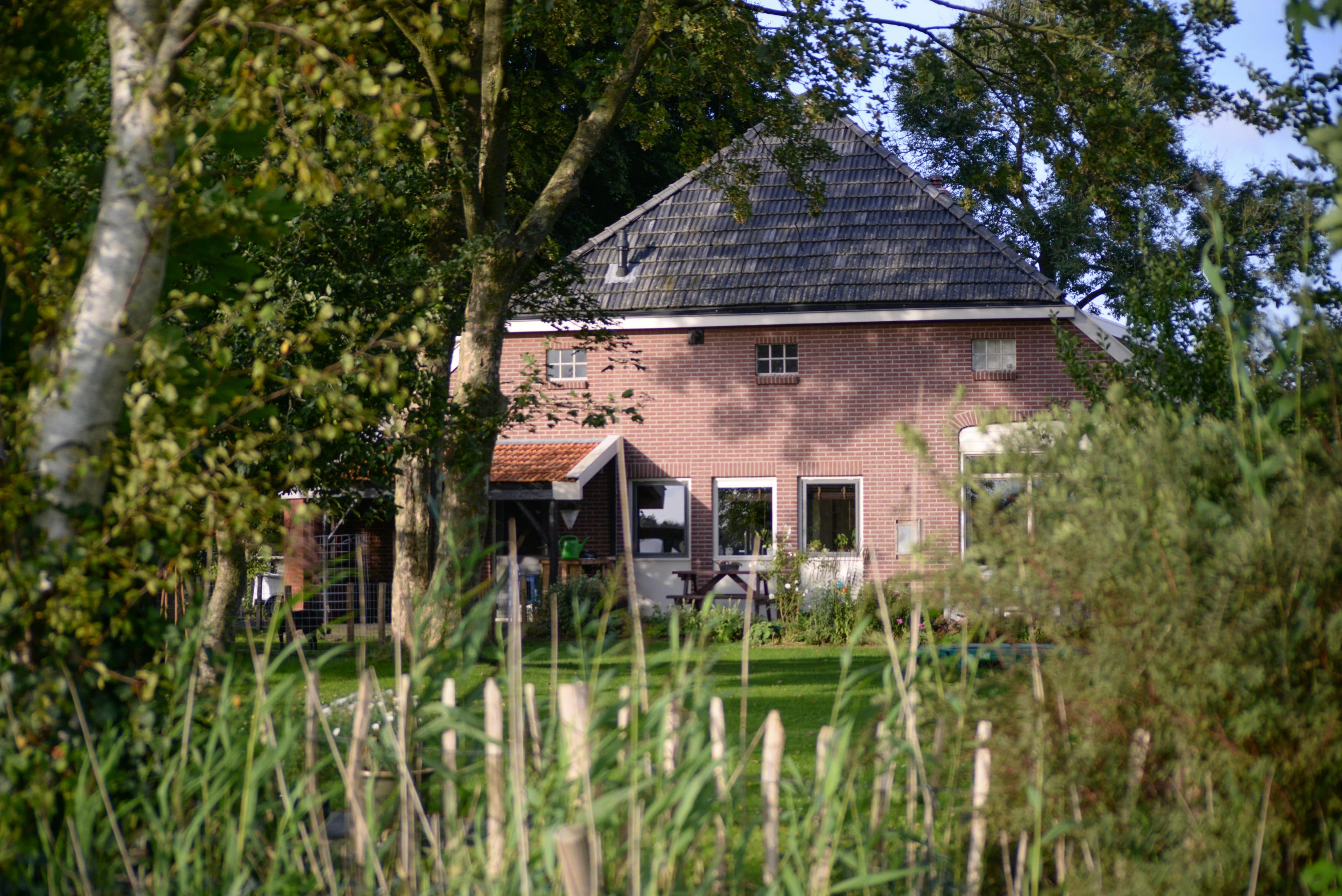 a house sitting on top of a lush green field, by Jan Tengnagel, happening, near pond, exterior photo, terracotta, ecovillage