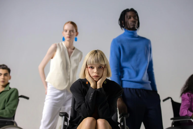 a woman sitting in a wheel chair in front of a group of people, trending on pexels, bauhaus, frown fashion model, issey miyake, on a mannequin. studio lighting, uniform off - white sky