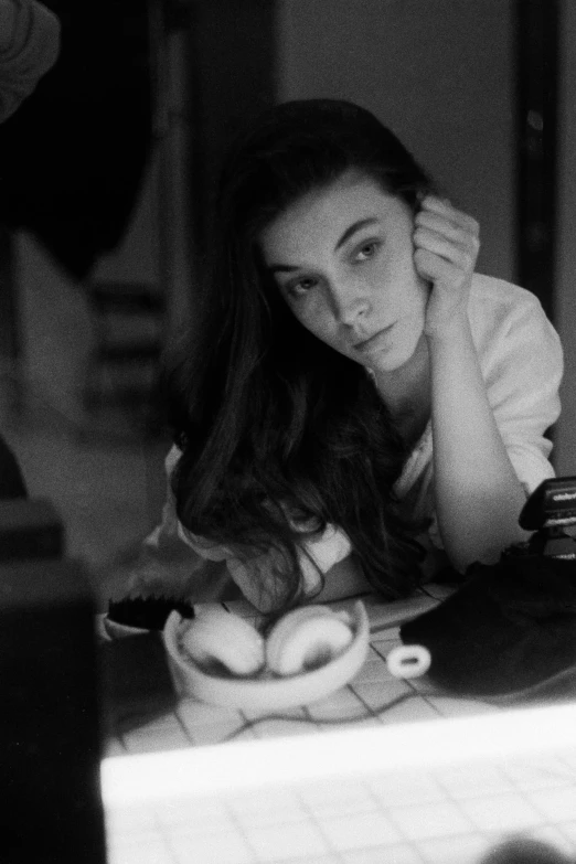 a black and white photo of a woman sitting at a table, a black and white photo, tumblr, photorealism, young woman with long dark hair, lofi, selfie, bjork