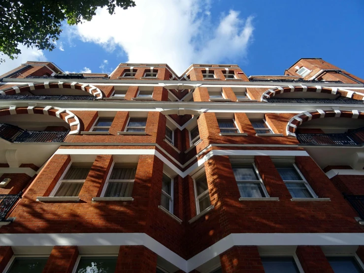 a tall brick building with many windows and balconies, by Jessie Algie, unsplash, art nouveau, blue sky above, ground level view, red bricks, ignant