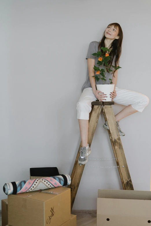 a woman sitting on top of a ladder next to boxes, inspired by Sarah Lucas, trending on pexels, aestheticism, decorated with flowers, jeans and t shirt, in a white boho style studio, a wooden