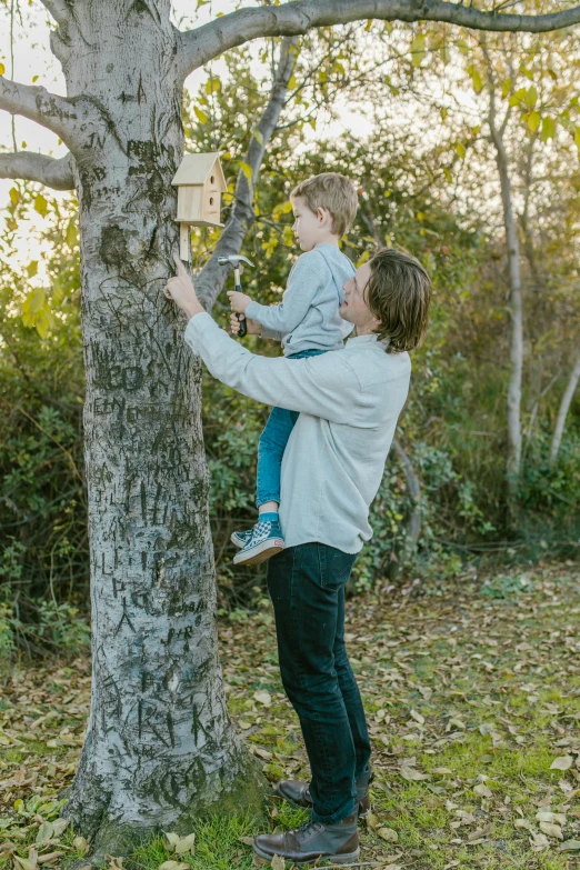 a woman holding a child up to a tree, by Will Ellis, unsplash, conceptual art, honey and bee hive, cardboard, with his pet bird, trail camera