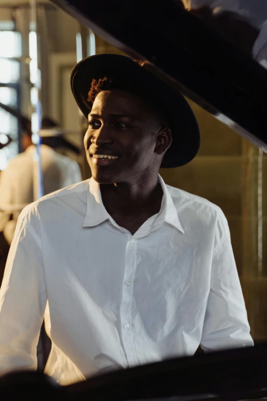 a man in a hat sitting in front of a piano, wearing a white button up shirt, dark skin, muzinabu, smiling confidently