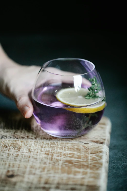 a person holding a glass with a lemon slice in it, inspired by Wlodzimierz Tetmajer, pexels, violet spike smoke, herbs, spherical, a purple fish