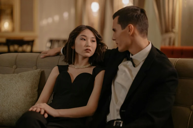 a man and a woman sitting on a couch, by Emma Andijewska, trending on pexels, art nouveau, asian girl, young female in black tuxedo, looking her shoulder, [ theatrical ]