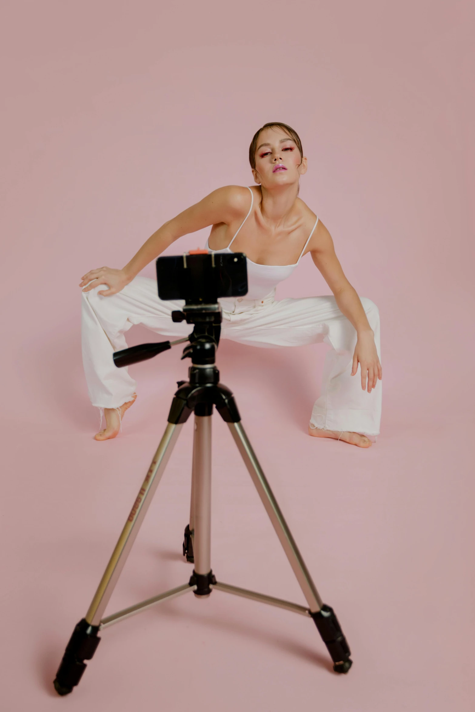 a woman sitting on top of a tripod next to a camera, tendu pose, sydney sweeney, holding it out to the camera, contorted