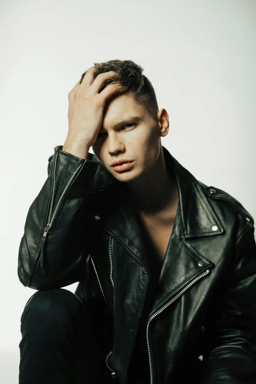 a man in a leather jacket sitting on the ground, an album cover, by Cosmo Alexander, trending on pexels, bauhaus, frown fashion model, big cheekbones, nonbinary model, headshot profile picture