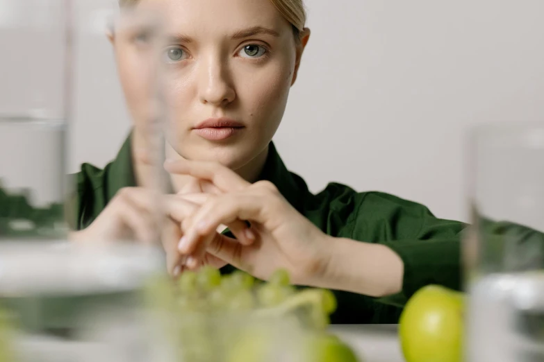 a woman sitting at a table with an apple in front of her, trending on pexels, hyperrealism, stood in a lab, concentrated look, close up of a blonde woman, woman made of plants