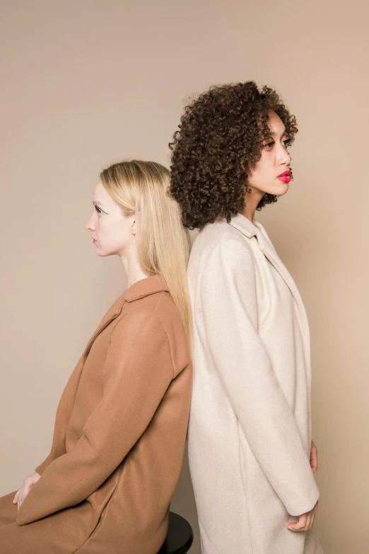 a couple of women sitting next to each other, inspired by Vanessa Beecroft, trending on pexels, curly blond hair, walking to the right, mixed-race woman, minimal palette