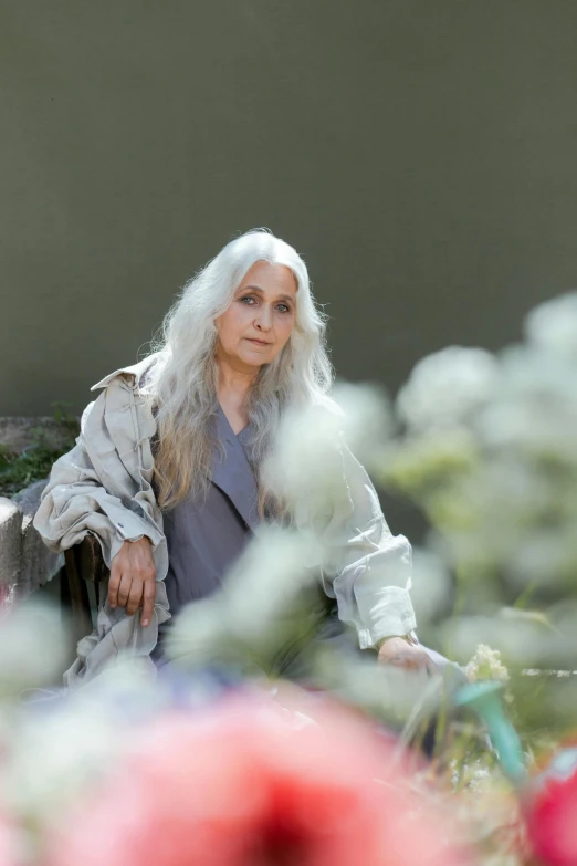 a woman sitting on a bench in a field of flowers, an album cover, inspired by Grethe Jürgens, renaissance, light gray long hair, portrait 6 0 - year - old woman, dayanita singh, intense look