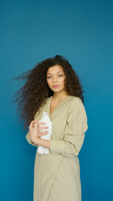 a woman standing in front of a blue wall holding a cell phone, an album cover, inspired by Esaias Boursse, pexels contest winner, renaissance, holding a white duck, a black man with long curly hair, mixed-race woman, water bottle queen