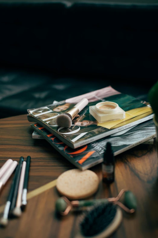 a magazine sitting on top of a wooden table, lots of makeup, art materials, cinematic image, small