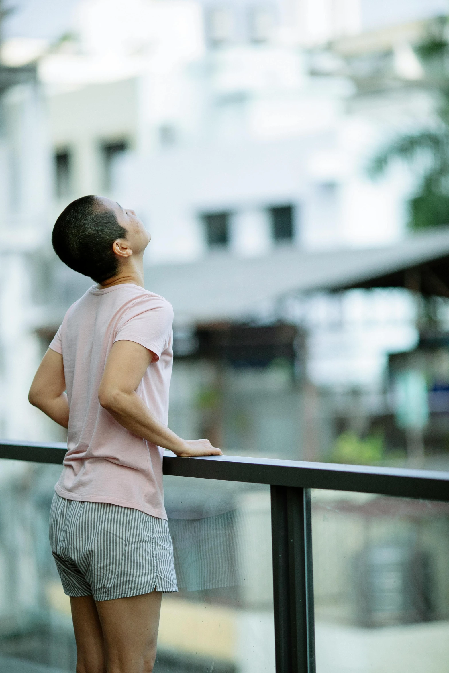 a man standing on top of a balcony next to a building, a picture, trending on unsplash, queer woman, shaven, asian woman, recovering from pain