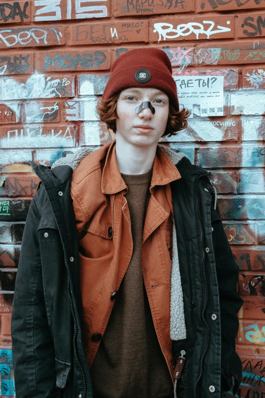 a man standing in front of a wall covered in graffiti, an album cover, trending on pexels, ginger hair with freckles, beanie, very pale skin, ((red)) baggy eyes