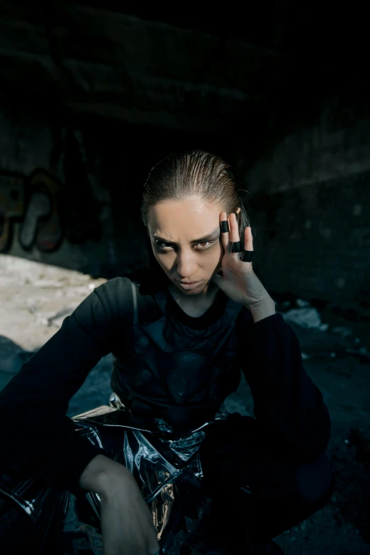 a woman sitting on the ground talking on a cell phone, an album cover, inspired by Elsa Bleda, trending on pexels, antipodeans, wearing techwear and armor, portrait androgynous girl, black clothing, headshot