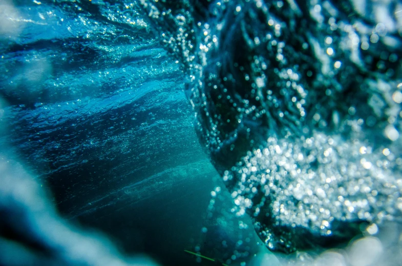 a close up of a wave in the ocean, a microscopic photo, by Niko Henrichon, pexels, bubbly underwater scenery, surfing a barrel wave, blue particles, bokeh ”