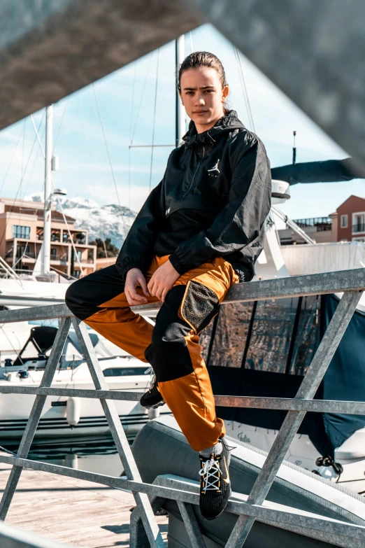 a man sitting on top of a boat on a dock, by Jan Tengnagel, photograph of a techwear woman, black and orange, cargo pants, caramel. rugged