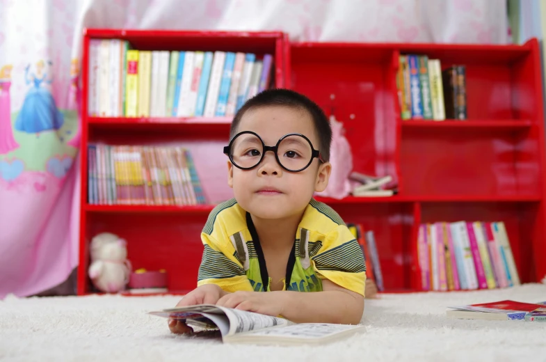 a young boy laying on the floor reading a book, a cartoon, by Bernardino Mei, pexels contest winner, shin hanga, square rimmed glasses, avatar image, looking confident, maintenance photo