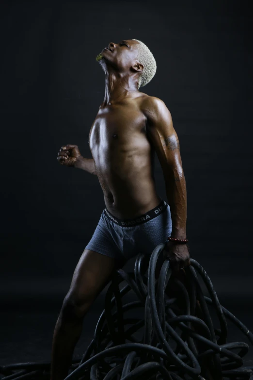 a man standing on top of a pile of wires, by Terrell James, art photography, muscular thighs, wheelchair, studio!! portrait lighting, nonbinary model
