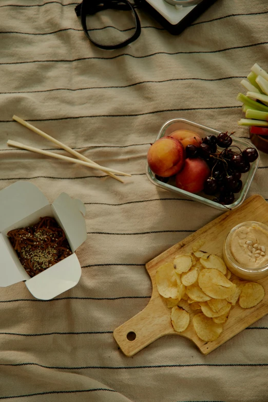 a wooden cutting board sitting on top of a bed, dau-al-set, snacks, humus, medium shot taken from behind, having a picnic