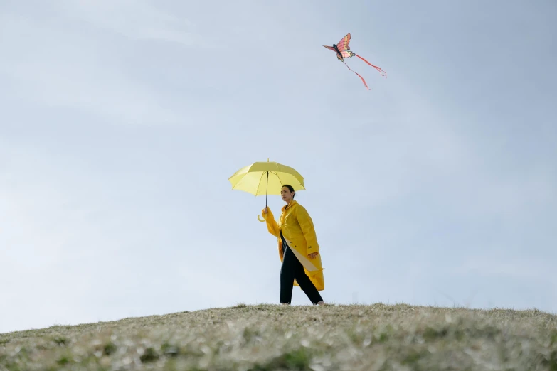 a person standing on a hill flying a kite, by Attila Meszlenyi, unsplash, yellow parasol, yellow raincoat, avatar image